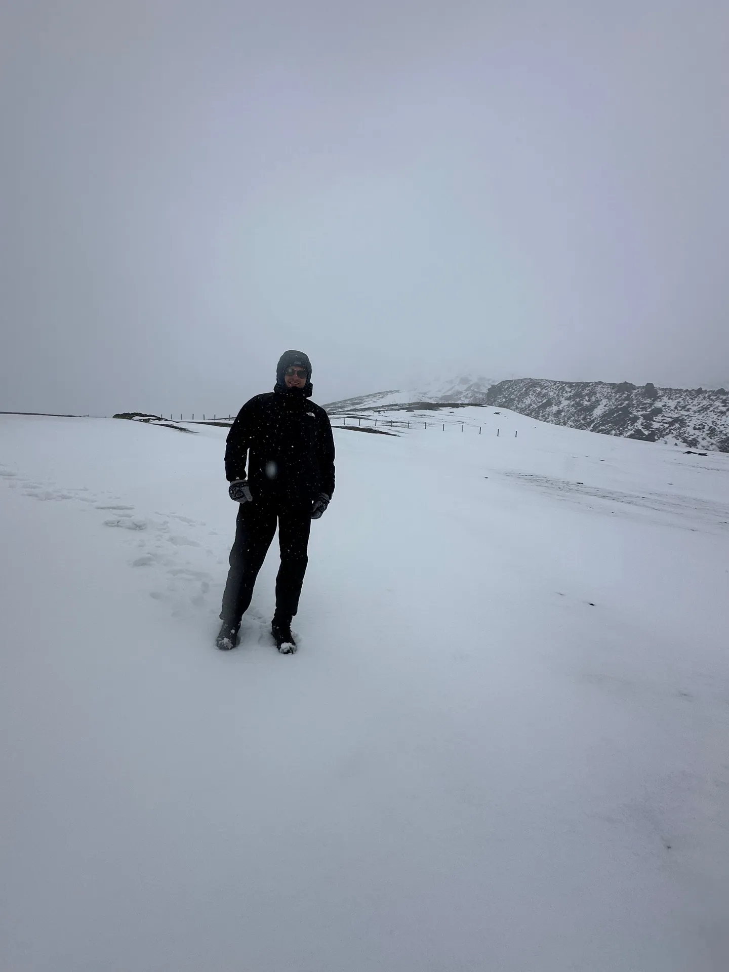 A climber walking through wind-blown snow on Cotopaxi’s upper slopes in bad weather