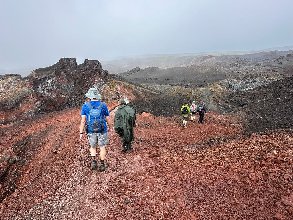 A group of hikers crossing the red and black lava fields of Sierra Negra volcano on Isabela Island, Galápagos